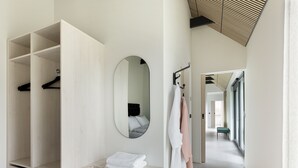 Un dormitorio moderno con vestidor, un espejo redondo y vistas a un pasillo con un banco.
