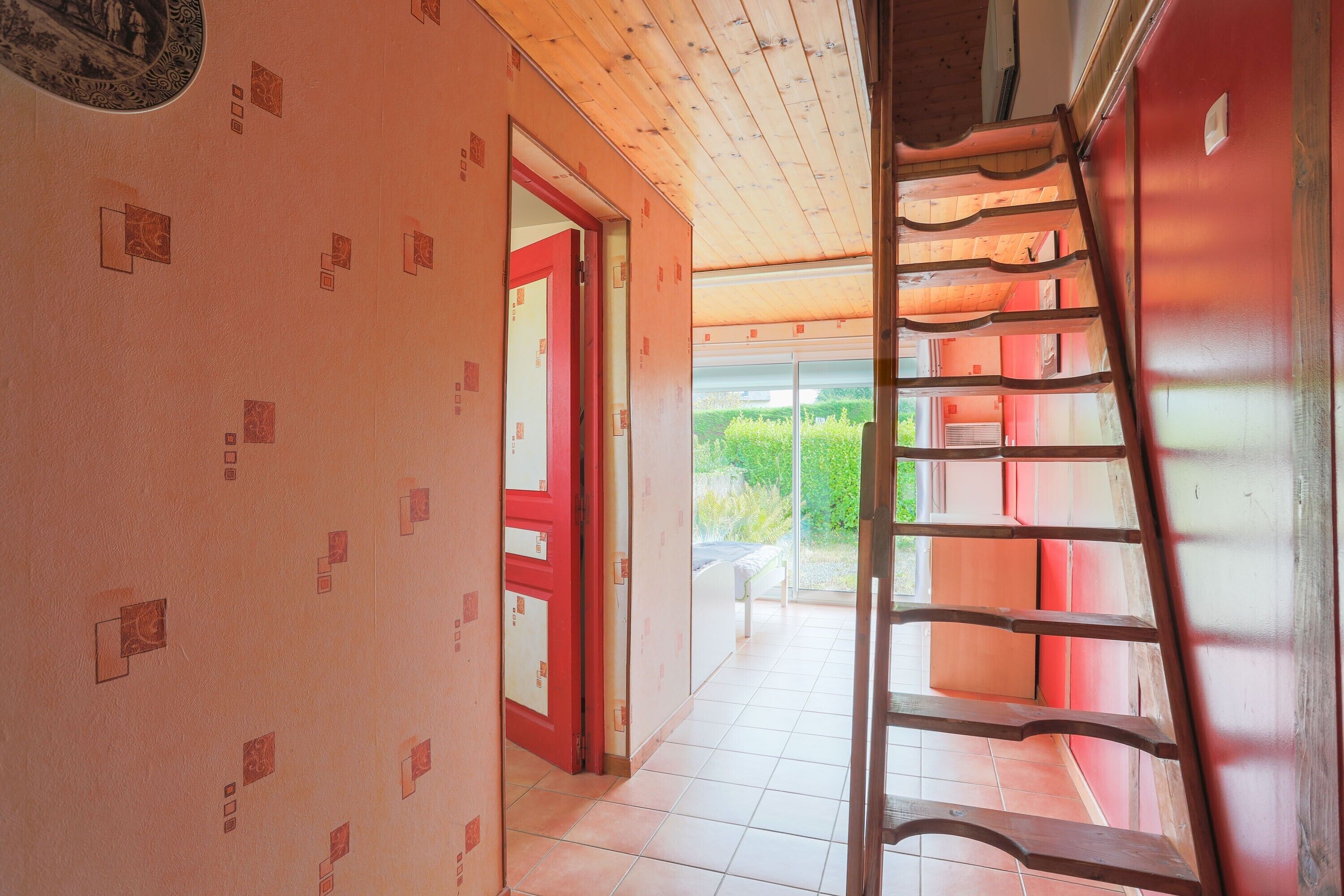 A corridor with a wooden ceiling, a red door, and a ladder against the wall.