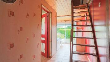 A corridor with a wooden ceiling, a red door, and a ladder against the wall.
