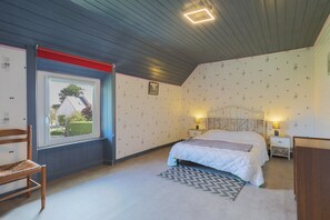 Un dormitorio con cama, mesitas de noche, una silla, un ventanal y un papel tapiz estampado.
