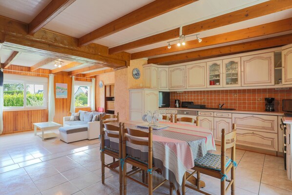 Une cuisine spacieuse avec des poutres en bois, des armoires blanches et un coin repas comprenant une table et des chaises.