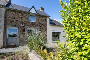 Une maison en pierre avec un jardin, un jardinière en bois et une fenêtre.