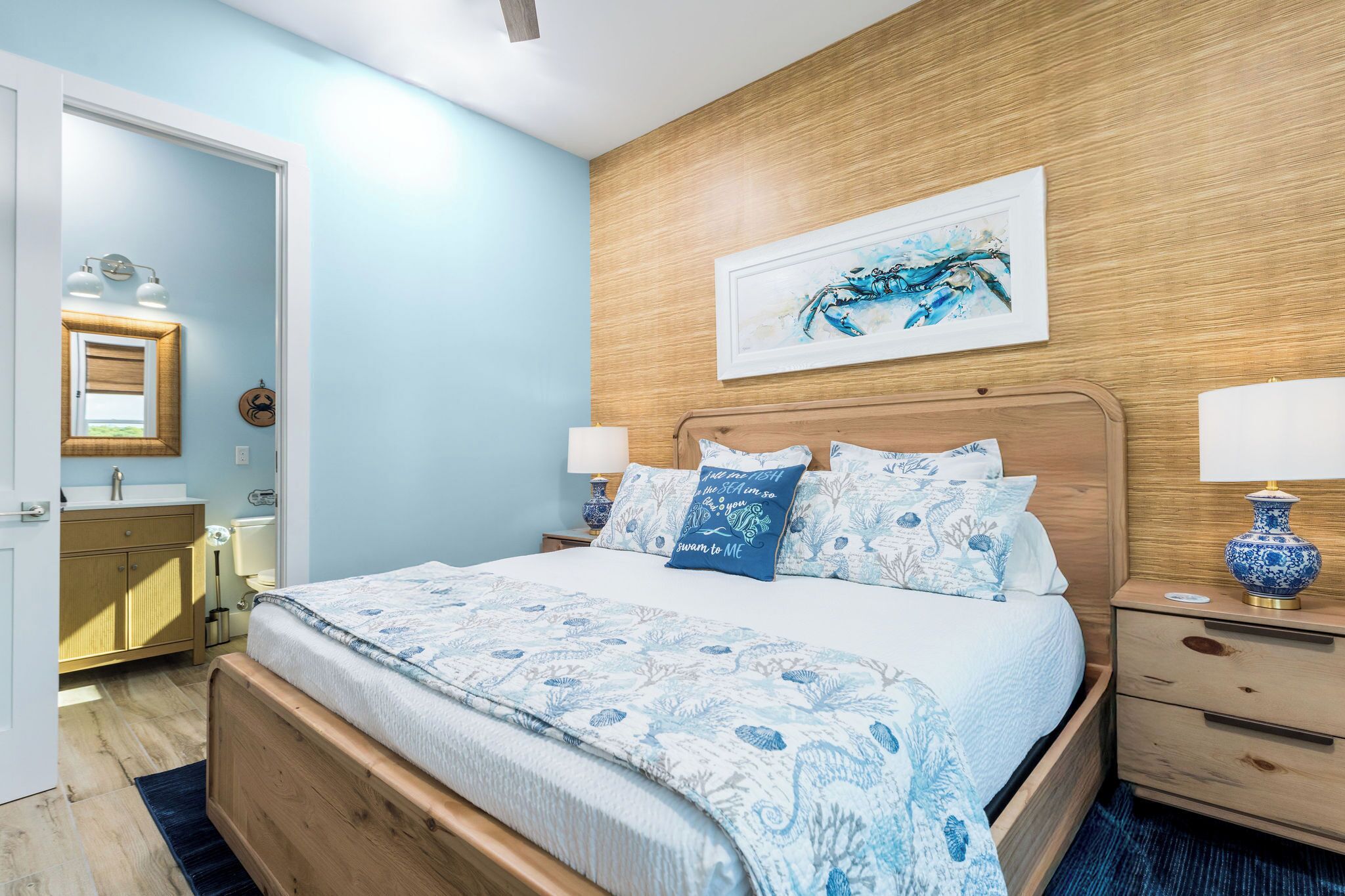 Un dormitorio con cabecera de madera, una cama grande con ropa de cama estampada, una mesita de noche con una lámpara y una obra de arte colgada en la pared.