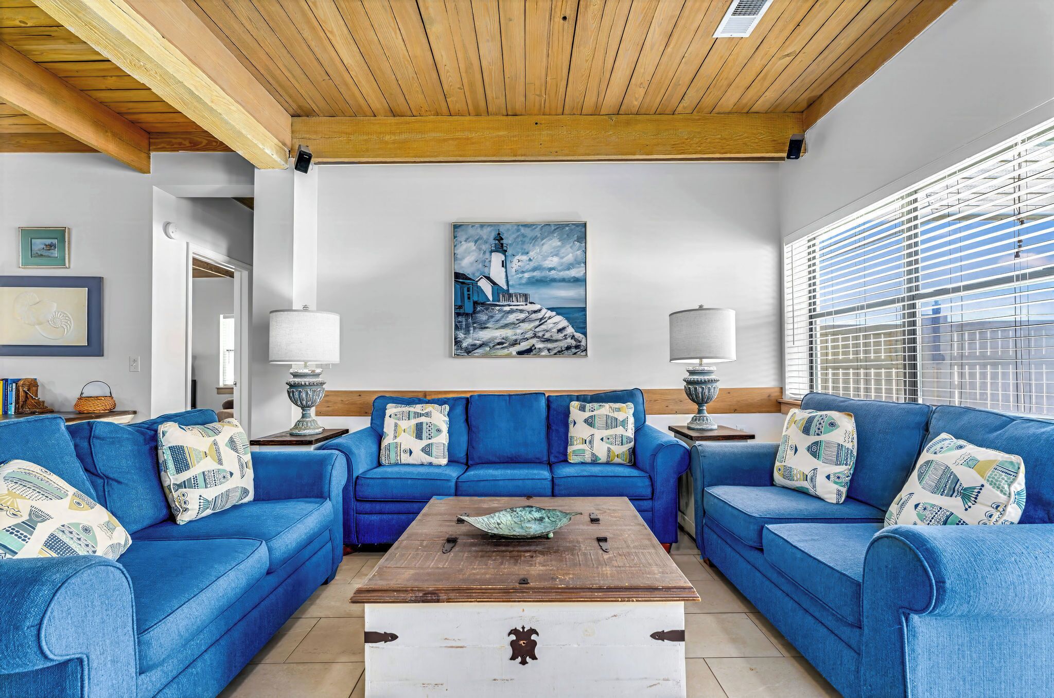 A living room with a blue sofa set, a wooden coffee table, and a painting of a lighthouse.