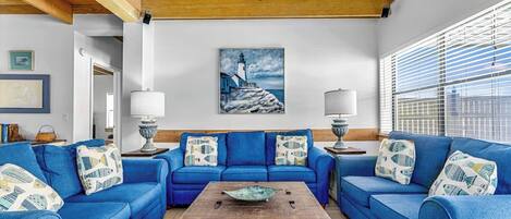 A living room with a blue sofa set, a wooden coffee table, and a painting of a lighthouse.