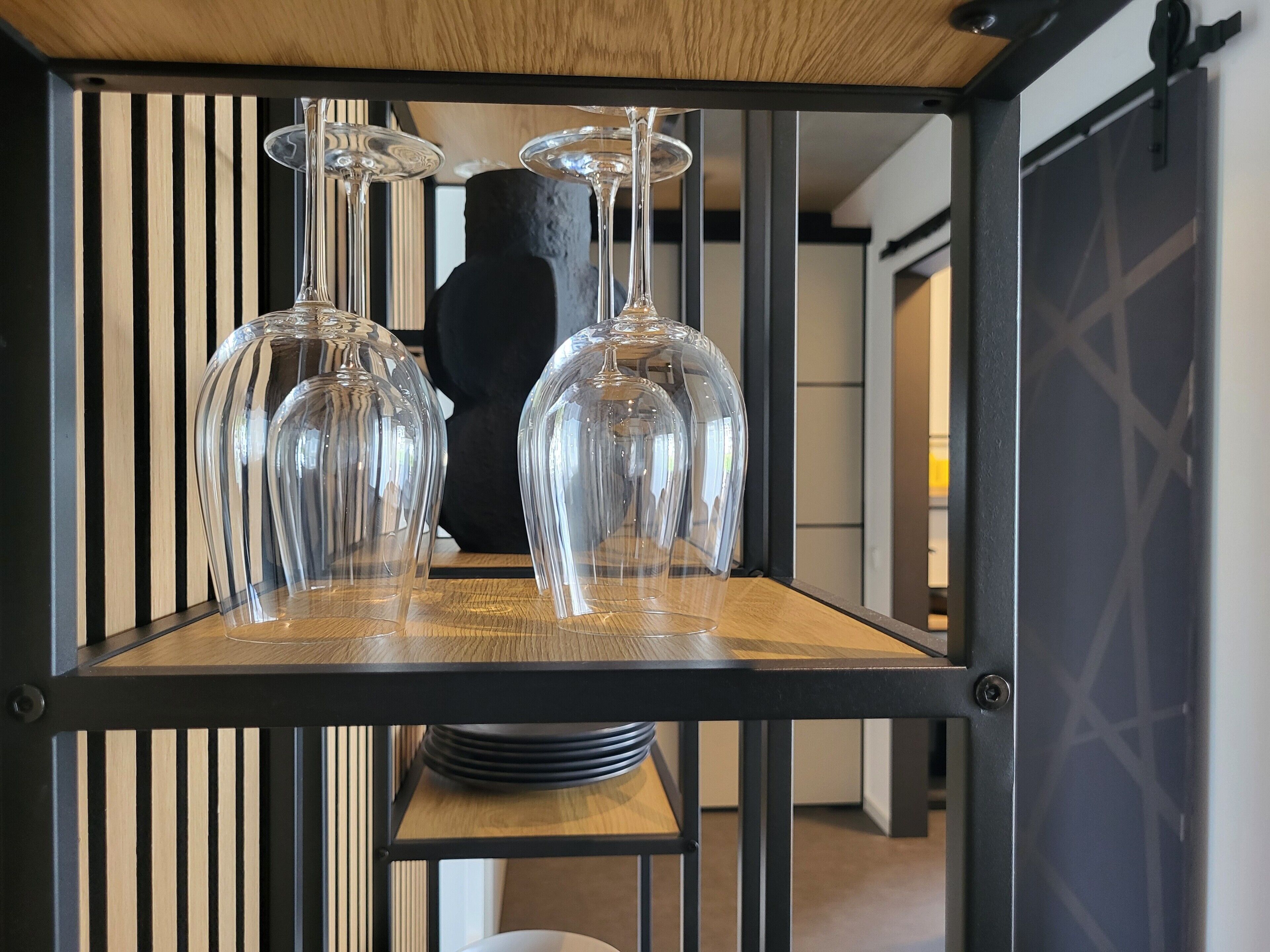 Un coin repas avec une table en bois, des verres à vin en verre transparent et un vase noir.