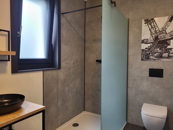 A bathroom with a shower, toilet, and a window.
