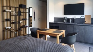 A modern room with a bed, a small wooden table, two chairs, a kitchen area, and a TV mounted on the wall. - Apartment 'Schlossterrassen 8b' with Private Terrace, Shared Garden and Wi-Fi (Muldestausee)