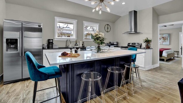 Una cocina moderna con una isla central, taburetes de bar, un refrigerador y una araña.