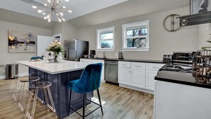 Una cocina moderna con una isla central, electrodomésticos de acero inoxidable y una silla azul.