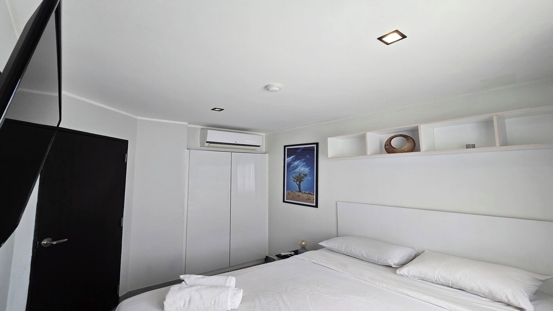 A modern hotel room with a large bed, a wardrobe, a mounted TV, and a framed picture on the wall.