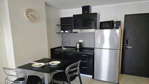 Una cocina compacta con encimera negra, electrodomésticos de acero inoxidable y un reloj en la pared.