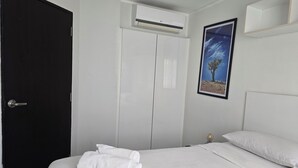 Habitación de hotel con una cama, ropa de cama blanca, una puerta negra, un armario blanco y un equipo de aire acondicionado.