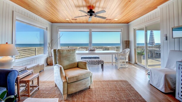 Een ruime kamer met een houten plafond en grote ramen met uitzicht op het strand.