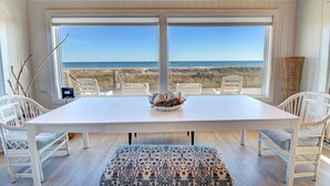 Een kamer met een groot raam met uitzicht op het strand, witte meubels en een zeegezicht.