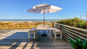 Een houten terras met een tafel, een bank en een parasol, met uitzicht op het strand en de zee.