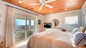 Een slaapkamer met een groot bed, een plafondventilator, een televisie en een balkon met uitzicht op de oceaan.