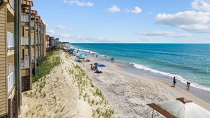 A beach with a wooden building on the left, a sandy shore, and a clear blue sky. - Enjoy oceanfront views from this 2BR condo at Topsail Dunes 3308 in North Topsail Beach. (North Topsail Beach)