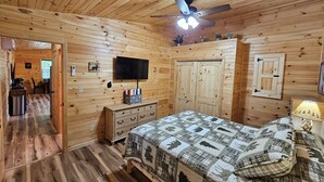 A wooden cabin bedroom with a bed, dresser, TV, and a ceiling fan. - Romantic Cozy Antler Cabin | Hot Tub + Fire Table (Murray)