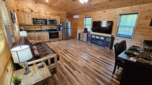 A cozy cabin-style kitchen with wooden floors, a dining area, and a TV. - Romantic Cozy Antler Cabin | Hot Tub + Fire Table (Murray)