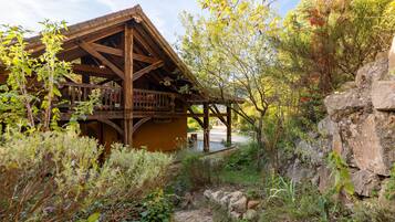 A rustic wooden cabin with a balcony, surrounded by natural vegetation and a rocky landscape.
