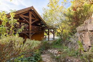 A rustic wooden cabin with a balcony, surrounded by natural vegetation and a rocky landscape.