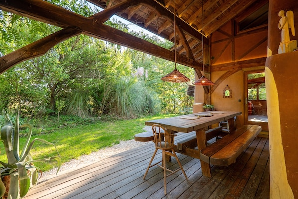 An outdoor wooden deck with a picnic table and benches, surrounded by lush greenery.