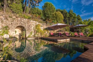 A stone bridge leading to a wooden deck with lounge chairs and umbrellas.