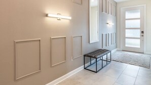 Un pasillo con iluminación empotrada, un banco y un tapete estampado que conduce a una puerta.