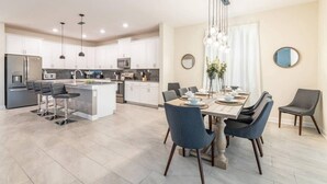 Una cocina moderna con armarios blancos, una isla central y un comedor con mesa y sillas.