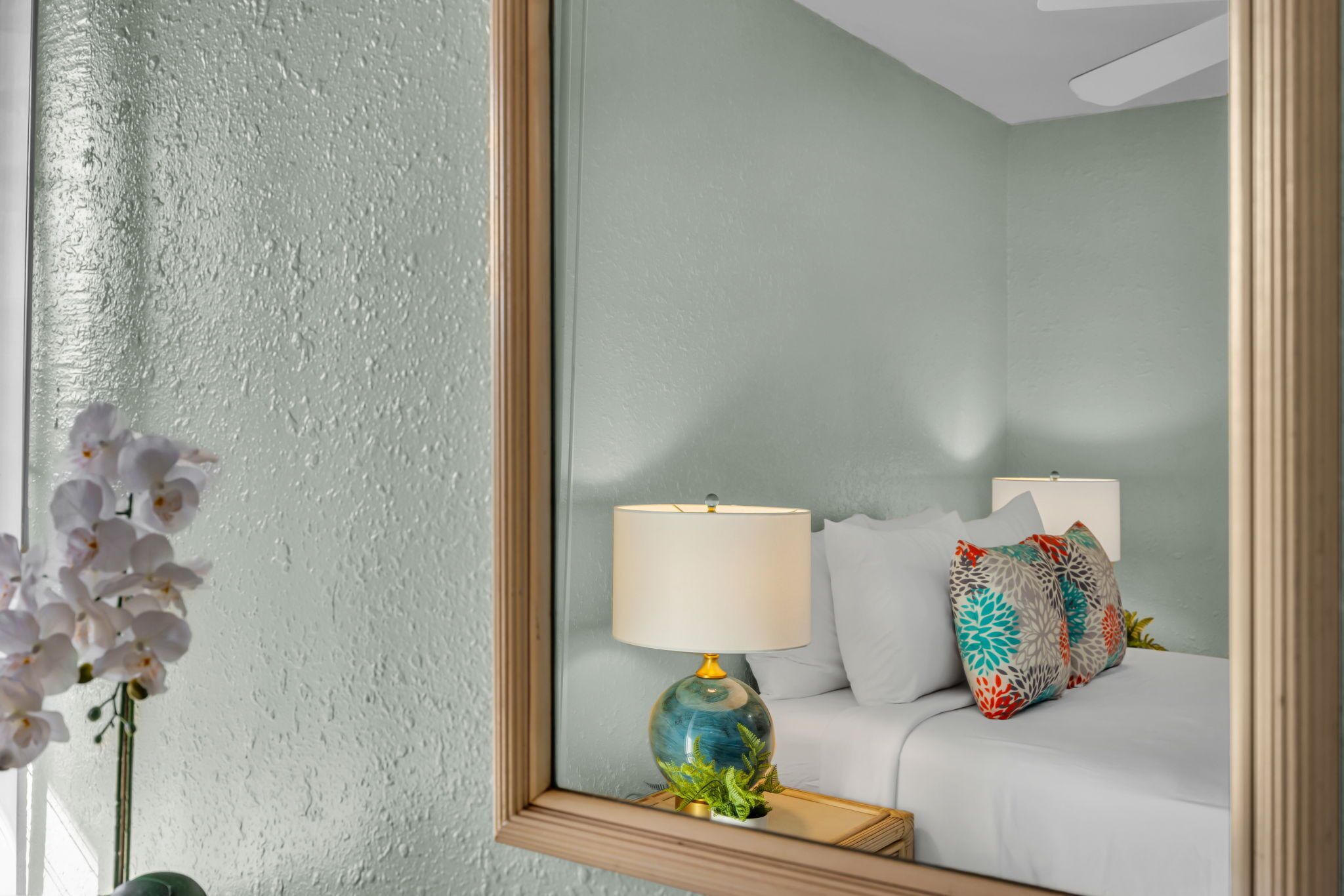 A bedroom with a bed, a bedside table with a lamp, and a mirror on the wall.