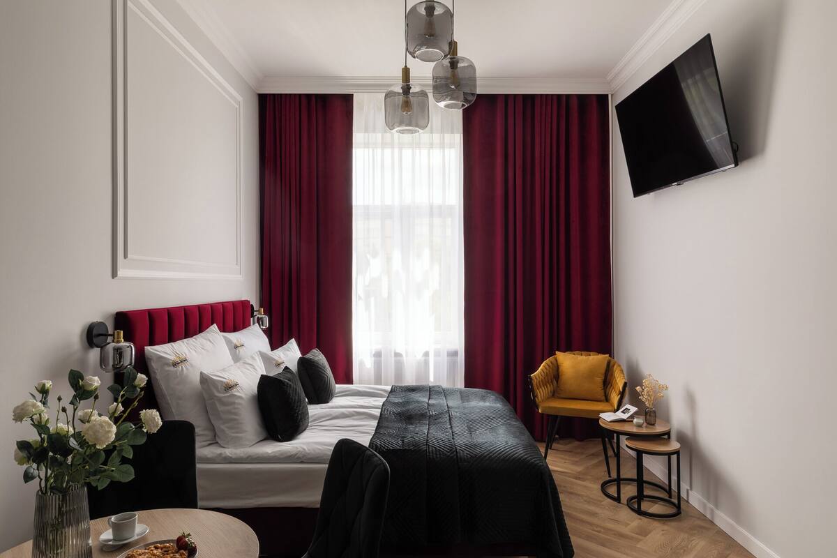 Una habitación de hotel moderna con una cama, una mesita con una taza y aperitivos, un sillón amarillo y un televisor montado en la pared.