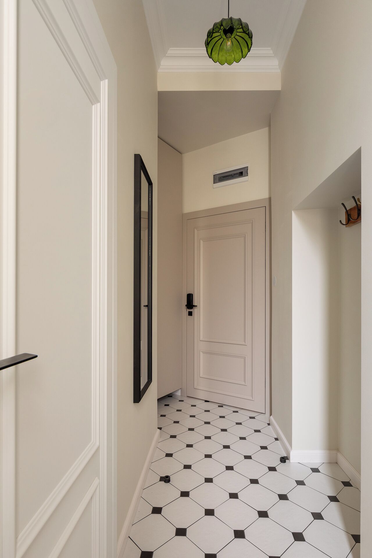 Corredor com porta branca, quadro pendurado na parede, luminária pendente verde e piso ladrilhado.