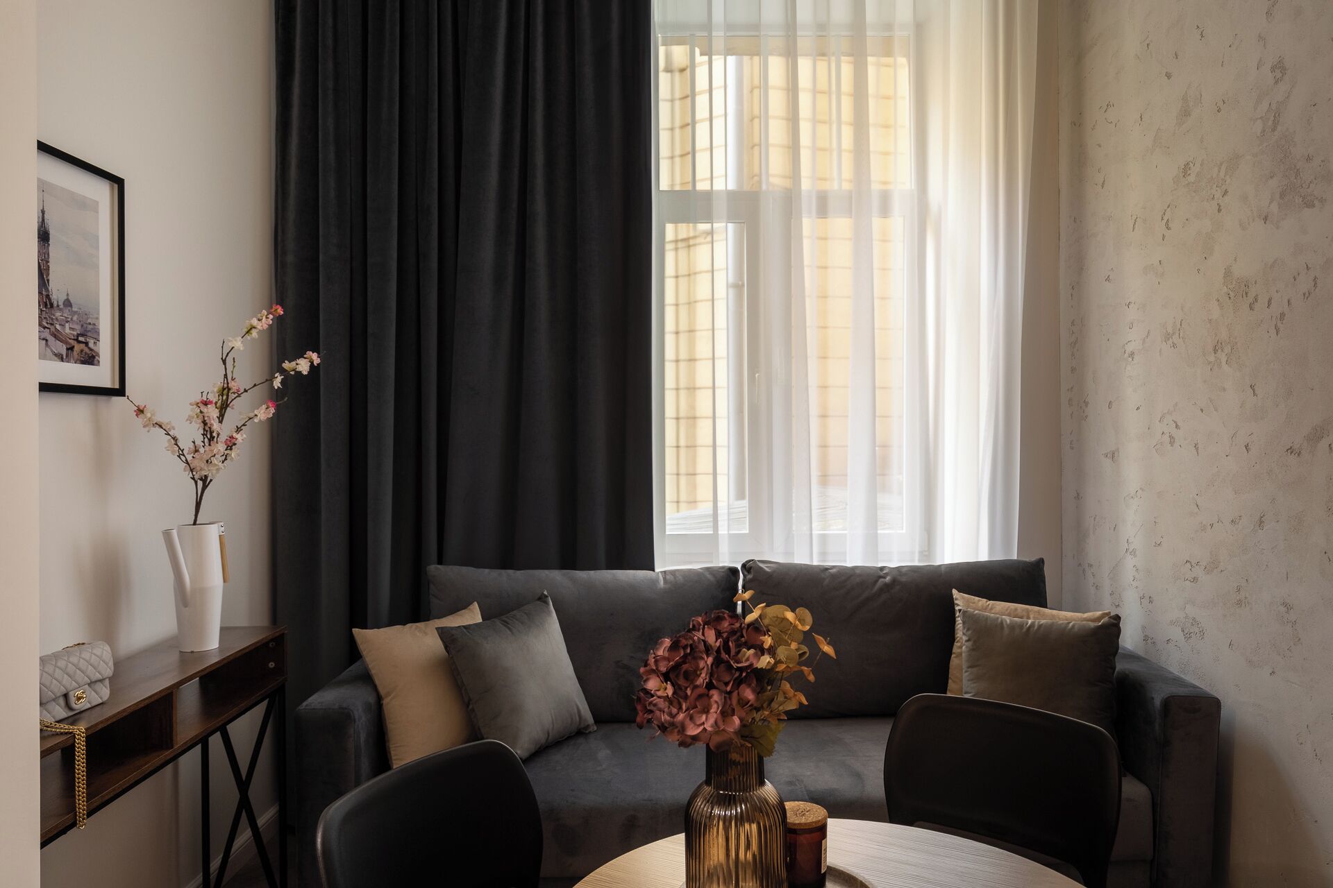 A modern living room with a dark grey sofa, a round wooden coffee table, and a vase with flowers.