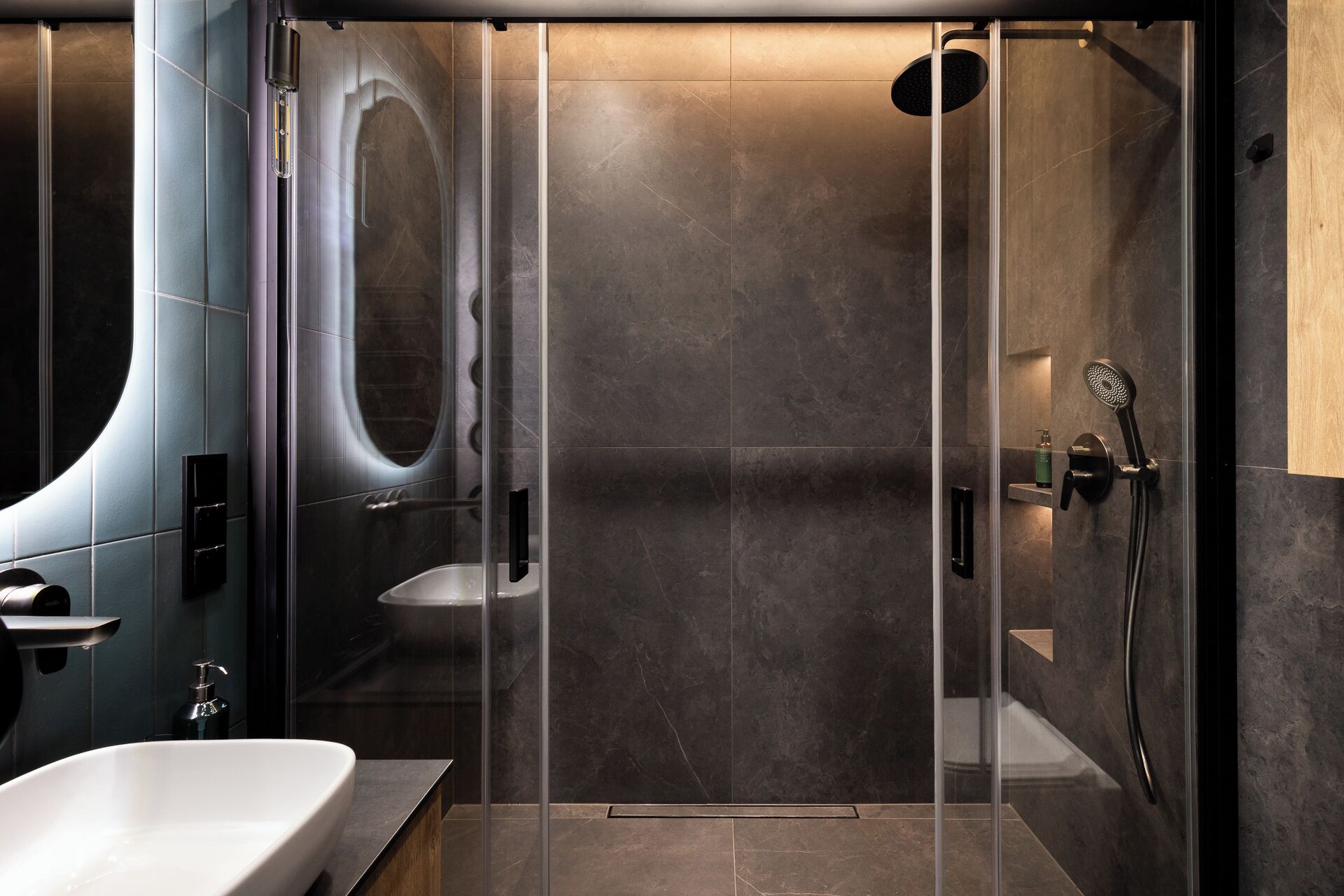 Un bany modern amb dutxa de vidre, banyera independent i un lavabo amb dosificador de sabó.