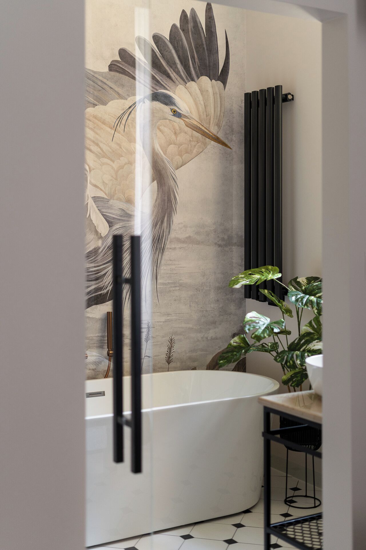 A modern bathroom with a freestanding bathtub, a large wall mural of a bird, and a potted plant.