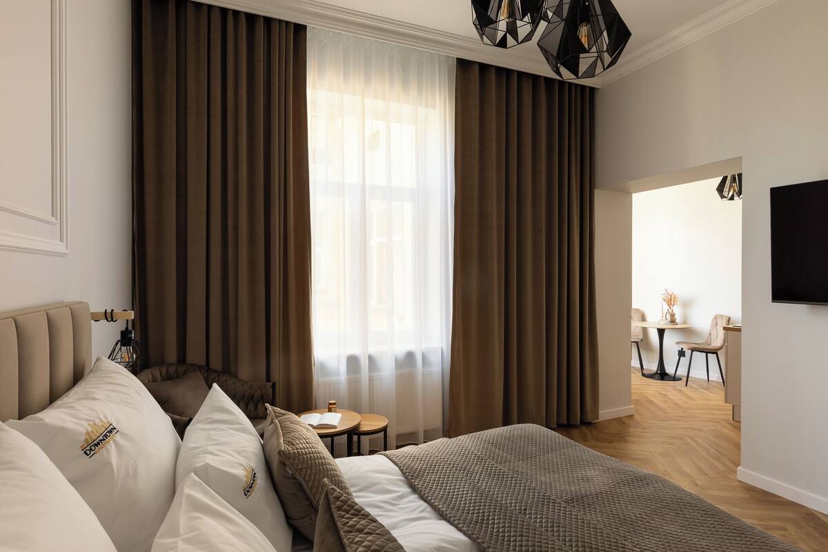 Habitación de hotel con una cama, una mesita con lámpara, un televisor y vista al pasillo.