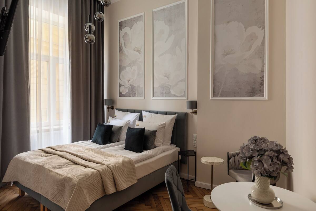Un dormitorio moderno con una cama grande, una mesita de noche con un florero y tres cuadros con motivos florales en la pared.