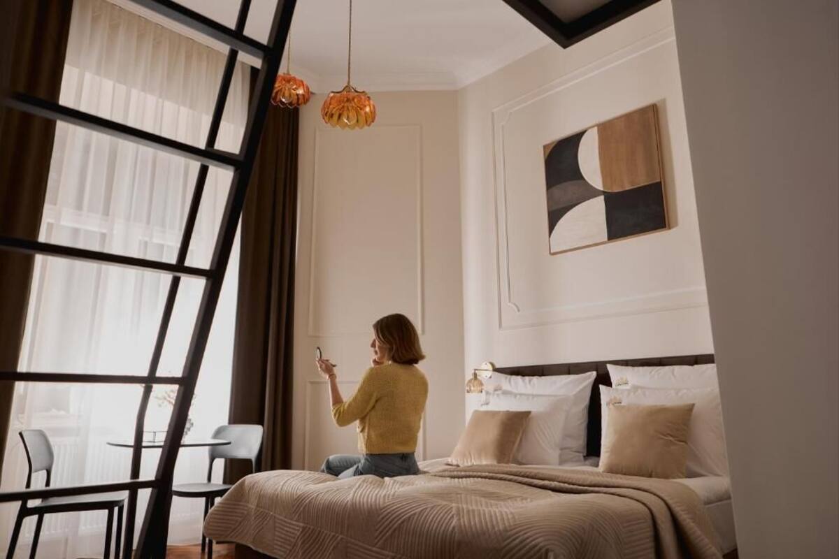 Una habitación con cama, ventana con cortinas, una mesa con sillas y una lámpara colgante.