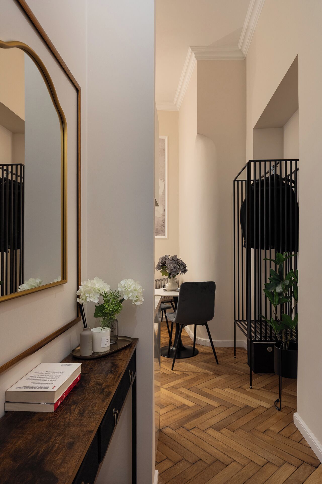 A hallway with a wooden floor, a black metal gate, a dining area with a table and chairs, and a mirror on the wall.