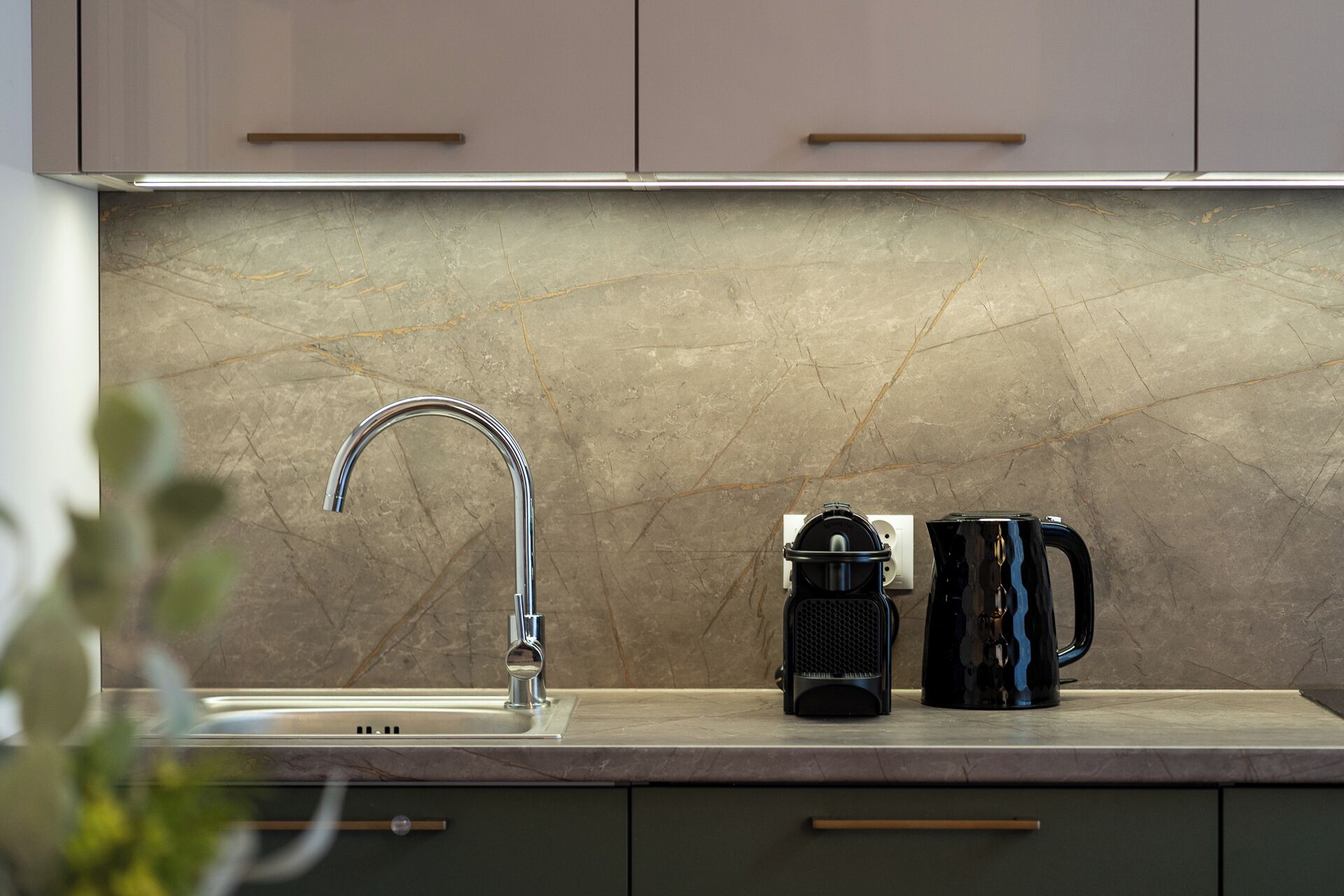 A kitchen with a single faucet, a coffee maker, and a kettle on the countertop.