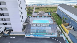 A rooftop pool area with a glass enclosure, lounge chairs, and a view of the beach. - Cozy Oceanfront Condo with Heated Pools & Views (Carolina Beach)