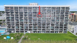 A multi-story hotel with balconies, a swimming pool, and a grassy area. - Cozy Oceanfront Condo with Heated Pools & Views (Carolina Beach)