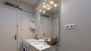 Une salle de bain moderne équipée d’un lave-linge intégré, d’un lavabo avec miroir et d’un porte-serviettes.