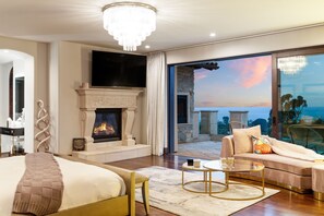 A modern bedroom with a fireplace, a large bed, a sofa, and a balcony with a view.