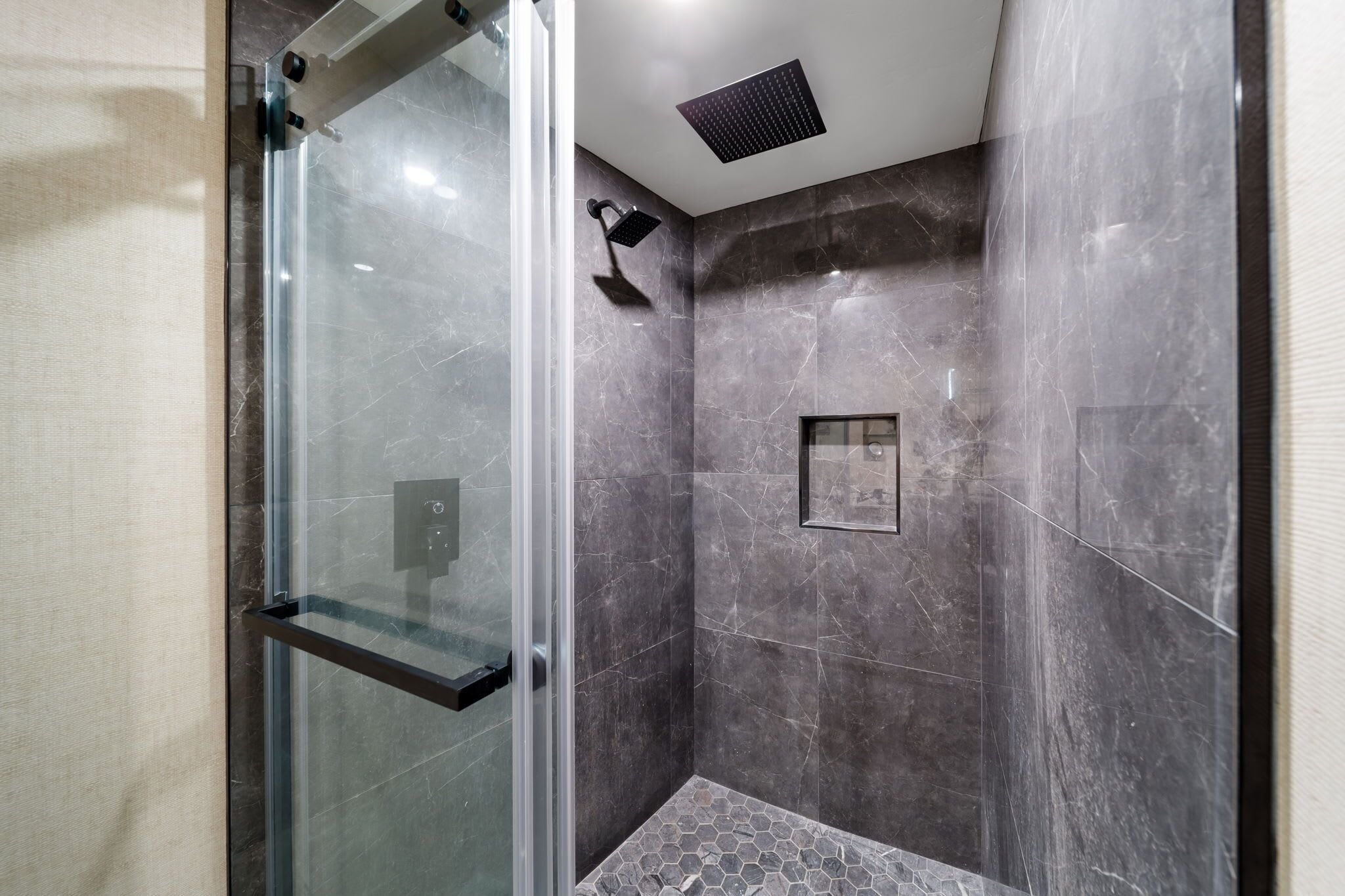 Un espace douche moderne avec une porte en verre, un pommeau de douche à main et un petit tableau encadré accroché au mur.