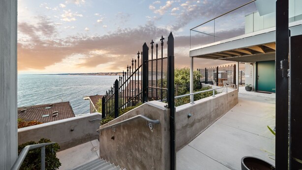 A modern outdoor staircase leading to a balcony overlooking a body of water, with a clear sky and distant cityscape. - New - Modern Studio - Stunning Ocean View (San Diego)