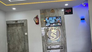 A reception area with a marble floor, a wooden reception desk, a digital clock, and a television on the wall. - Hotel S S Town (Vadodara)
