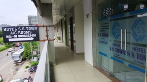 A hotel entrance with a sign indicating A/C rooms, a balcony with a view of the street, and a tiled floor. - Hotel S S Town (Vadodara)