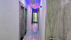 A hallway with marble walls and a reflective floor, leading to a room with a door at the end. - Hotel S S Town (Vadodara)